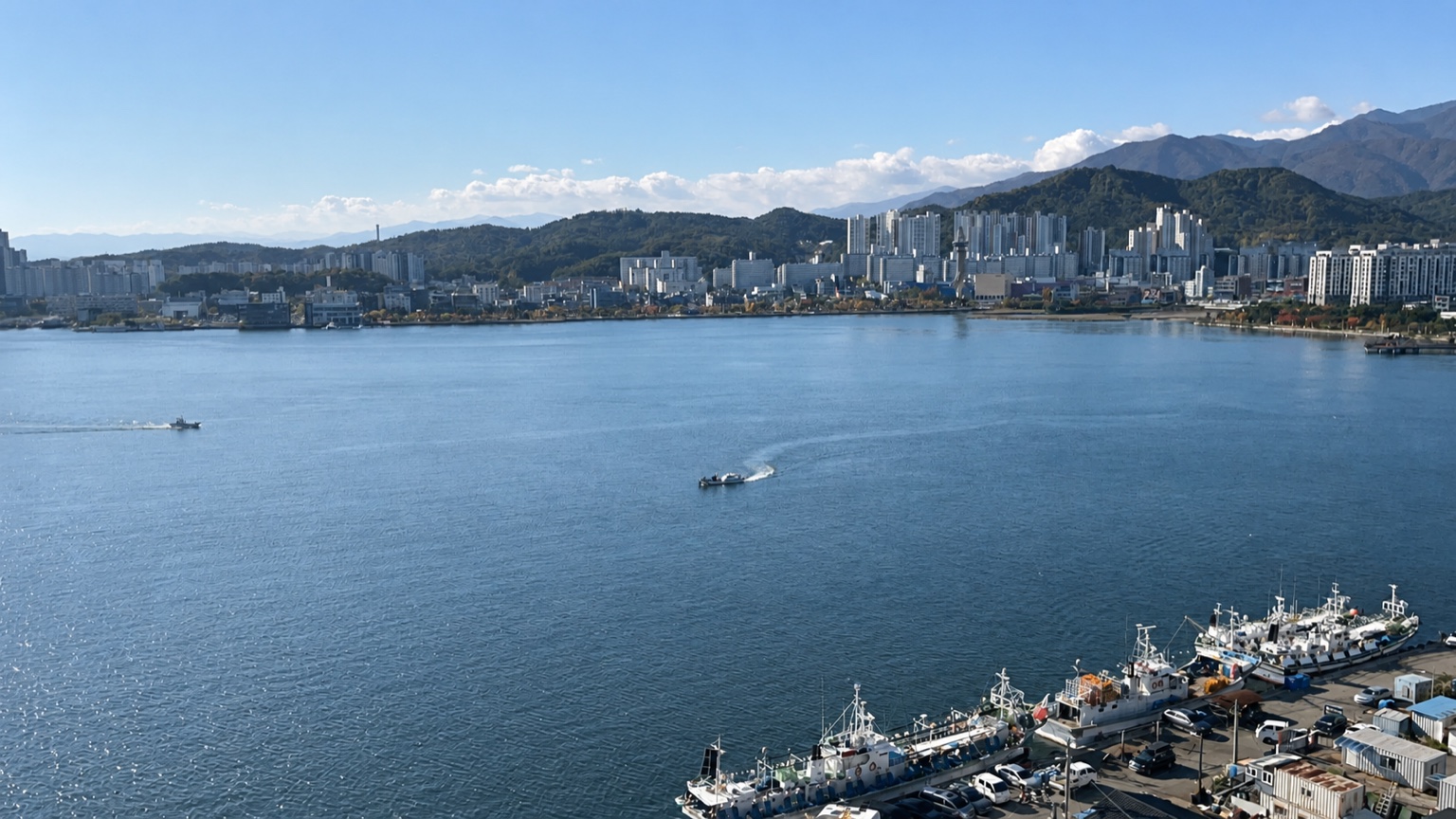 A wide harbour with boats, waterfront buildings and mountains