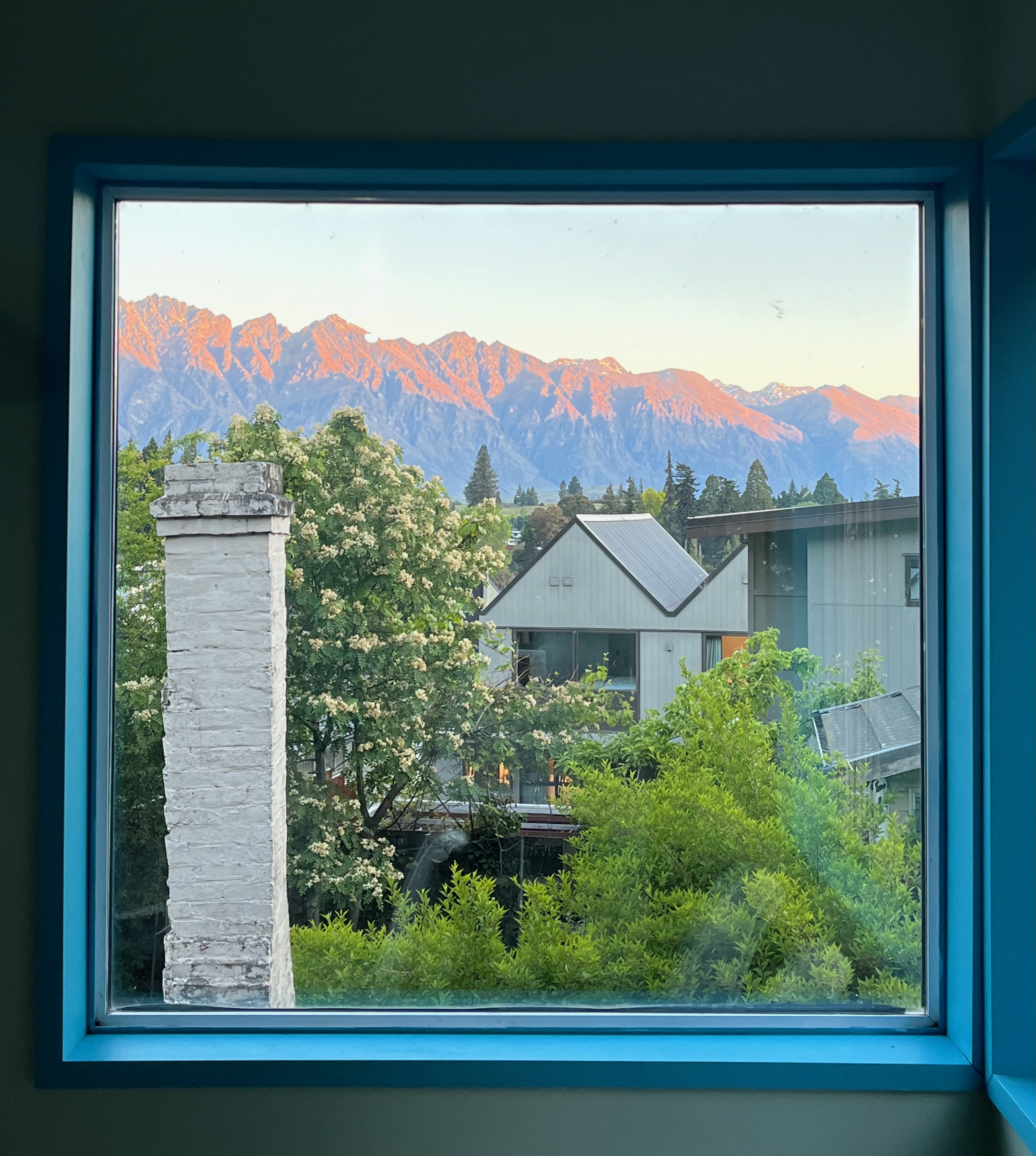 Queenstown mountains glowing at sunset through a blue-framed window